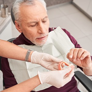 Dentist handing dentures to man in maroon shirt with gray hair